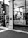 A black and white photograph depicts the storefront of a cafe called 'The Caffeinery' with a large logo featuring a coffee pot. The window is filled with words related to coffee and bakery items. It's located in a brick building, and nearby is a street sign and a lamppost.