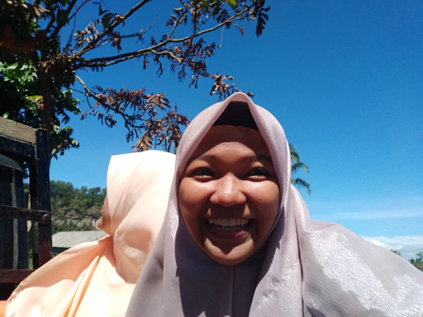 Close-up of a smiling athlete adjusting her terracotta-colored hijab outdoors with soft morning light.