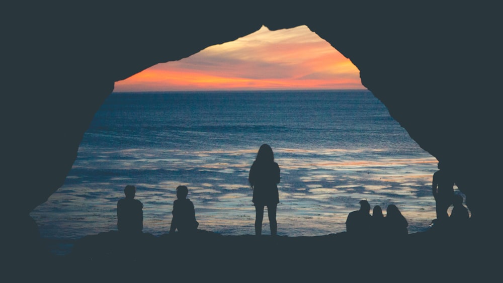 silhouette of people sitting on seashore watching sunset