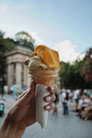 Hand holding a waffle cone filled with layered mango and passion fruit gelato.