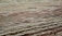 Layers of sedimentary rock formations with varying colors and textures are exposed on the surface. The patterns consist of red, brown, and gray hues, reminiscent of geological activity and erosion over time. The ground has a rugged, uneven appearance with visible stratification, indicating a rich geological history.