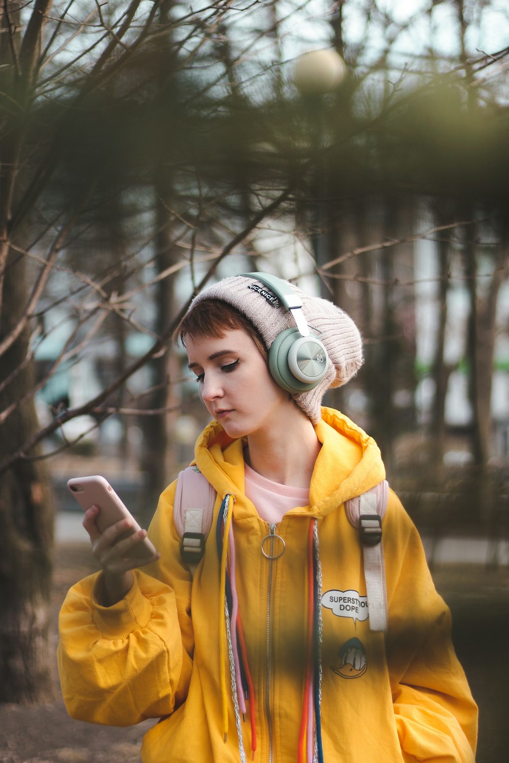 girl wears knit cap and yellow jacket holding smartphone