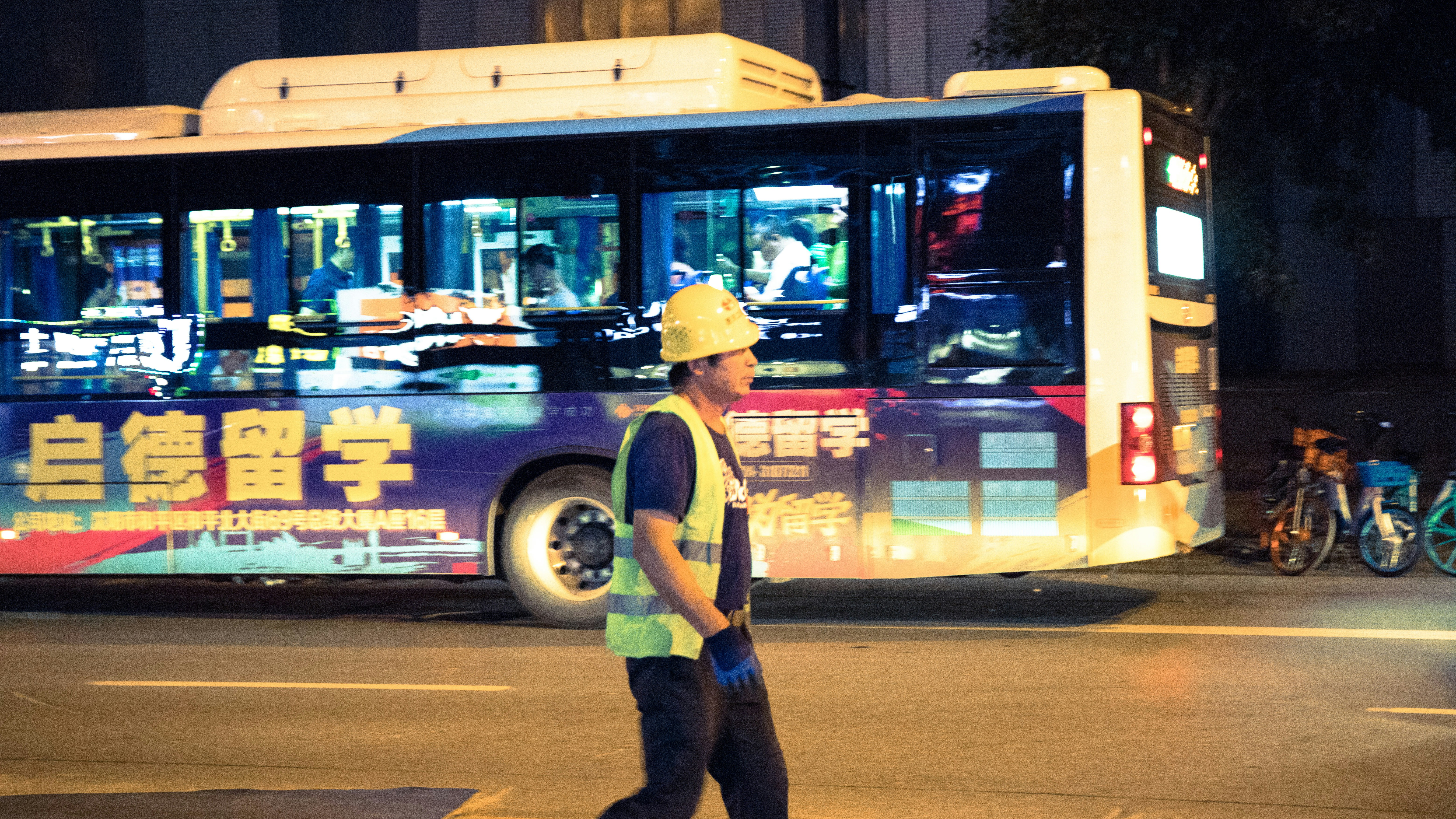 man wearing hard hat walking beside the road with bus