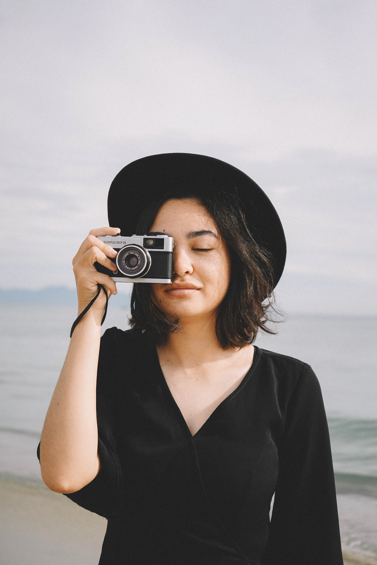 Woman holding a vintage camera near the shoreline.