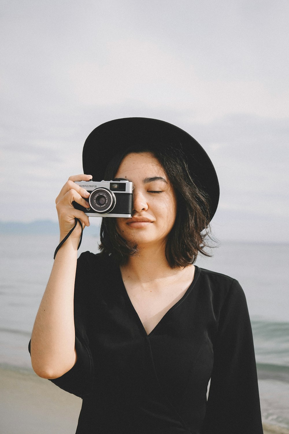 woman holds camera near to her right eye at the beach