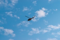 A Bell 505 helicopter in flight against a clear blue sky.