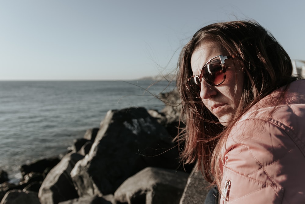 a woman in a pink jacket looking at the ocean