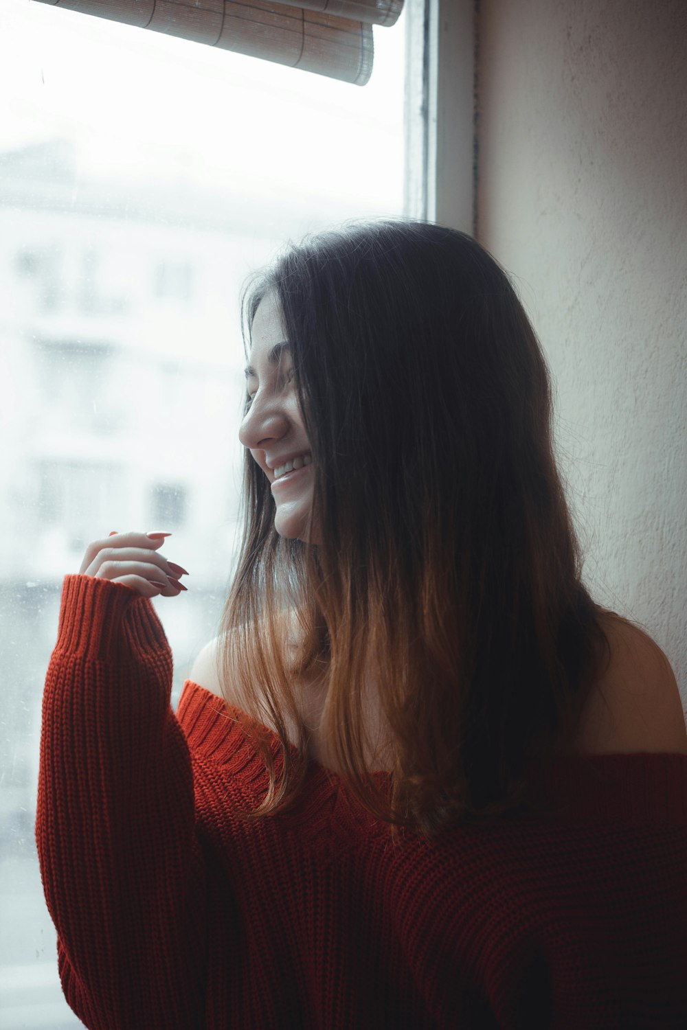 smiling woman in red off-shoulder sweater looking outside window