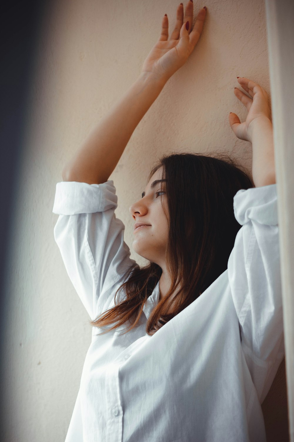 donna che indossa una camicia bianca appoggiata al muro