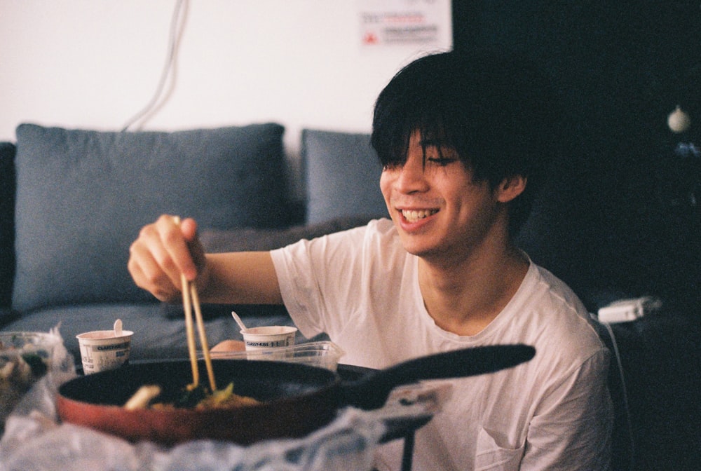 man using chopsticks to pickup food from pan