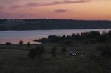 A scenic view of a car parked by a serene lake during sunset.
