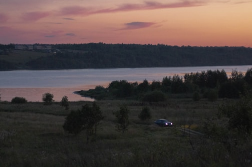 A serene lakeside villa at sunset with a vintage car parked nearby.