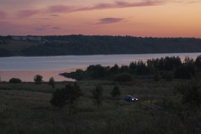 A scenic view of a car parked by a serene lake during sunset.