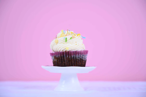 A close-up of a pale pink and white minimalist cake topper resting atop a beautifully frosted cupcake.