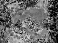 A detailed fresco painting depicts a celestial scene filled with mythological figures, including cherubic children and deities, surrounded by clouds and a lush tree. Intricate architectural elements and classical motifs frame the artwork, while various figures engage in dynamic poses.