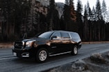 black GMC SUV passing road beside green pine trees during daytime