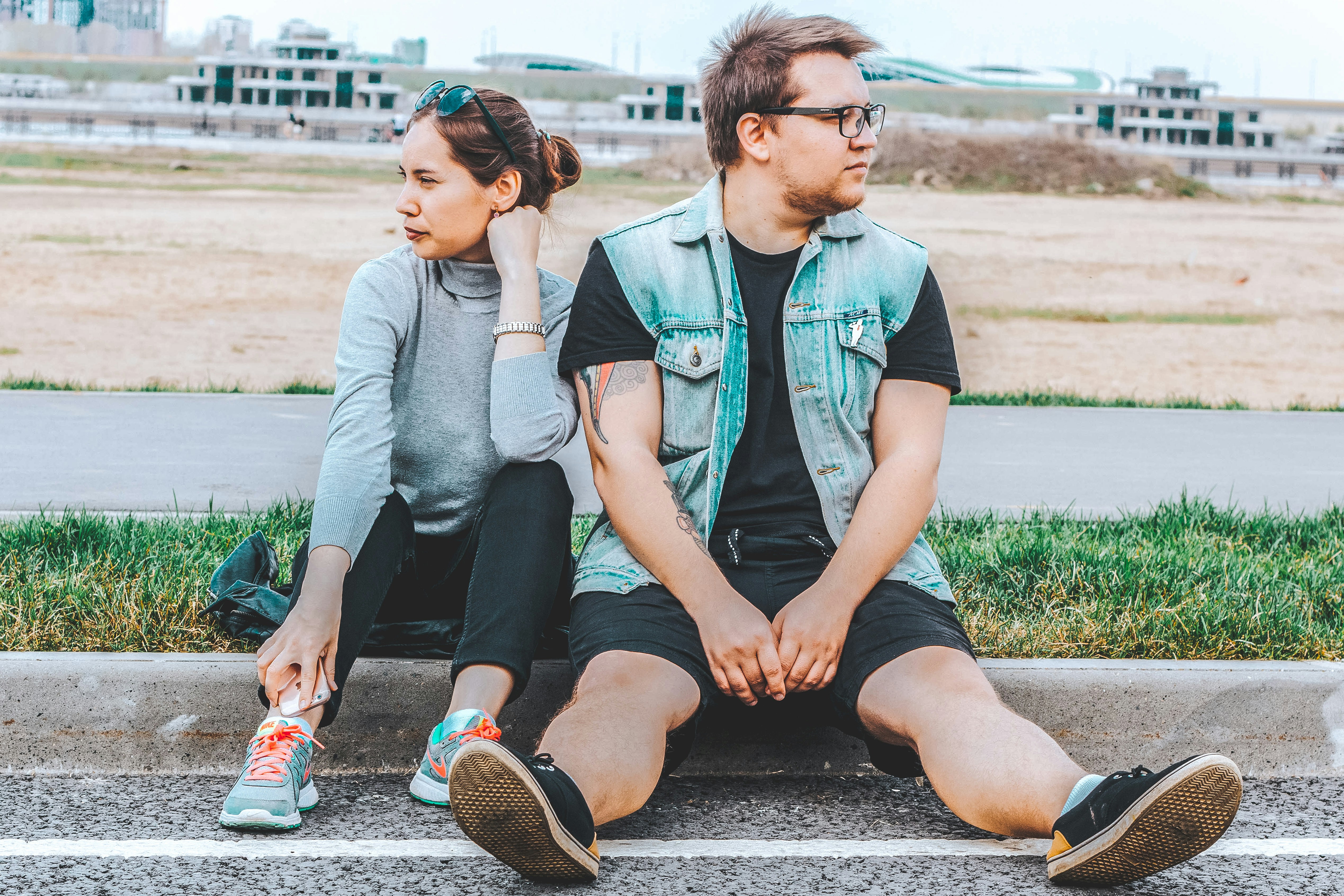 woman looking at her right sitting at curb beside man looking at his left