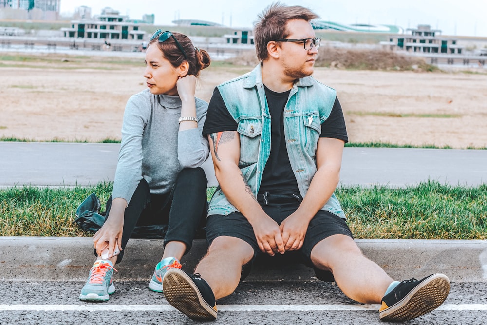 woman looking at her right sitting at curb beside man looking at his left