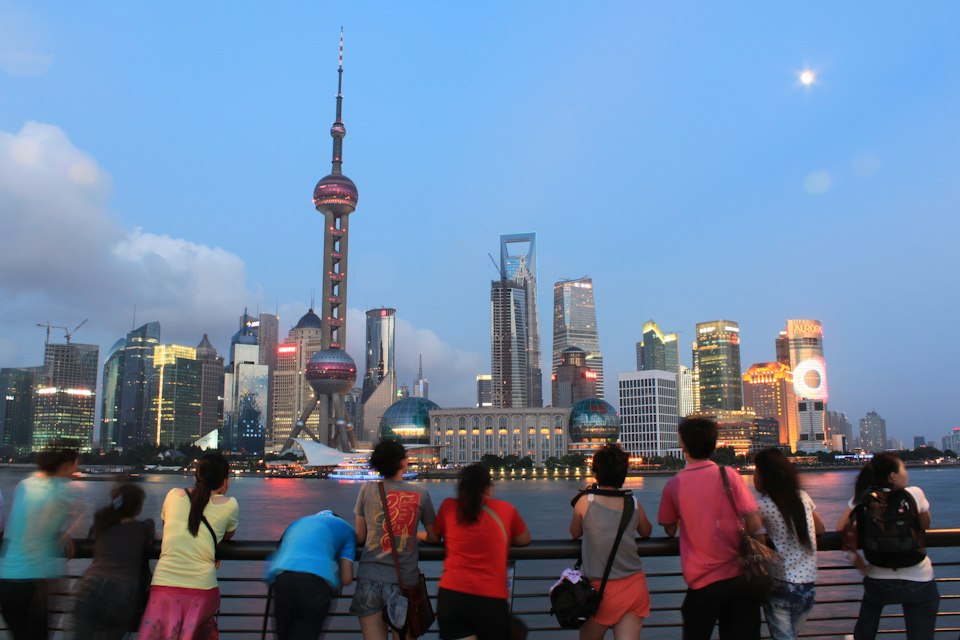 Visitors strolling the Bund promenade in daylight along Shanghai's colonial-era waterfront buildings