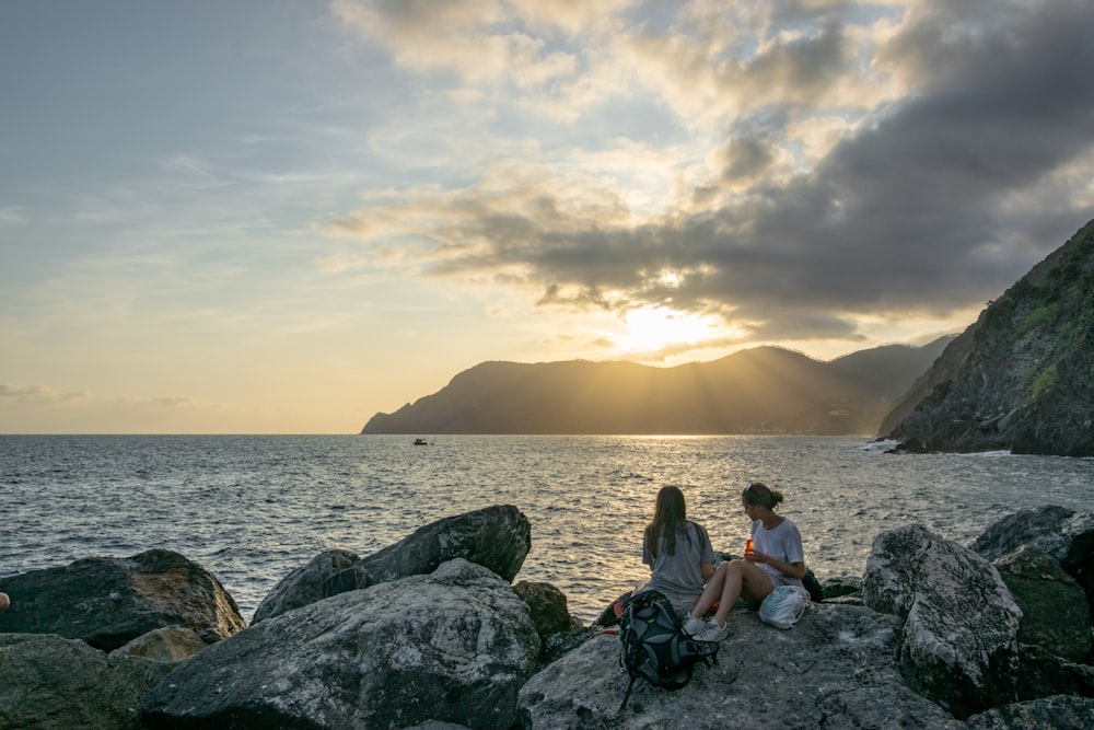 two women on rocks by the body of water