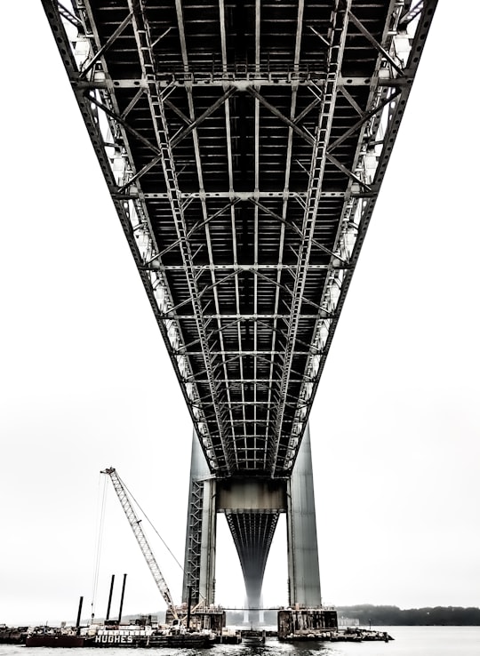 boats under black metal bridge at daytime in Verrazzano-Narrows Bridge United States