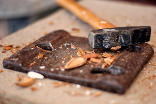Close-up of a vintage hammer resting on a wooden workbench with scattered nails.