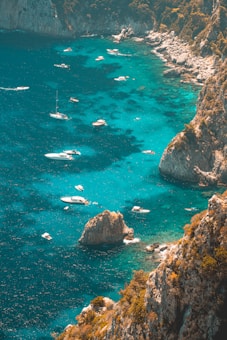 Several boats float on clear turquoise water near rocky cliffs and lush greenery.