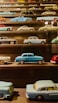 A neatly arranged collection of vintage miniature toy cars displayed on a wooden shelf.