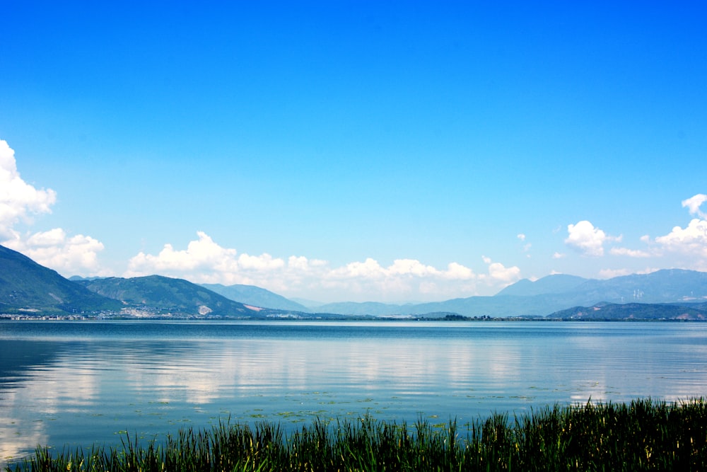 Gewässer in der Nähe von Hügeln unter weißen Wolken und blauem Himmel während des Tages