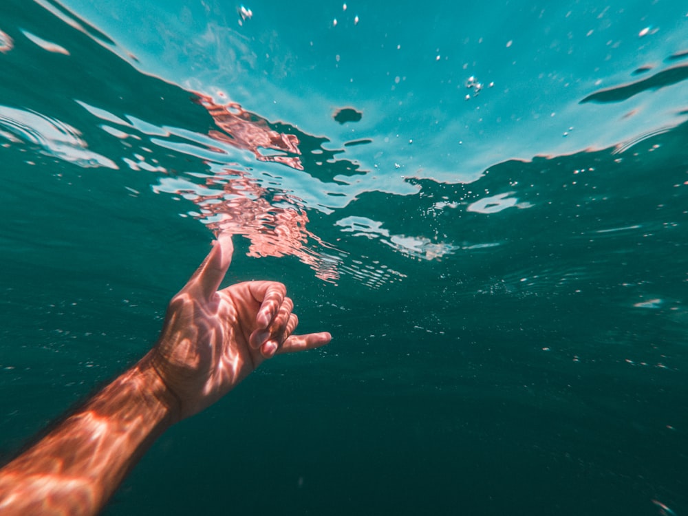 person doing hang loose gesture with their left hand underwater during day