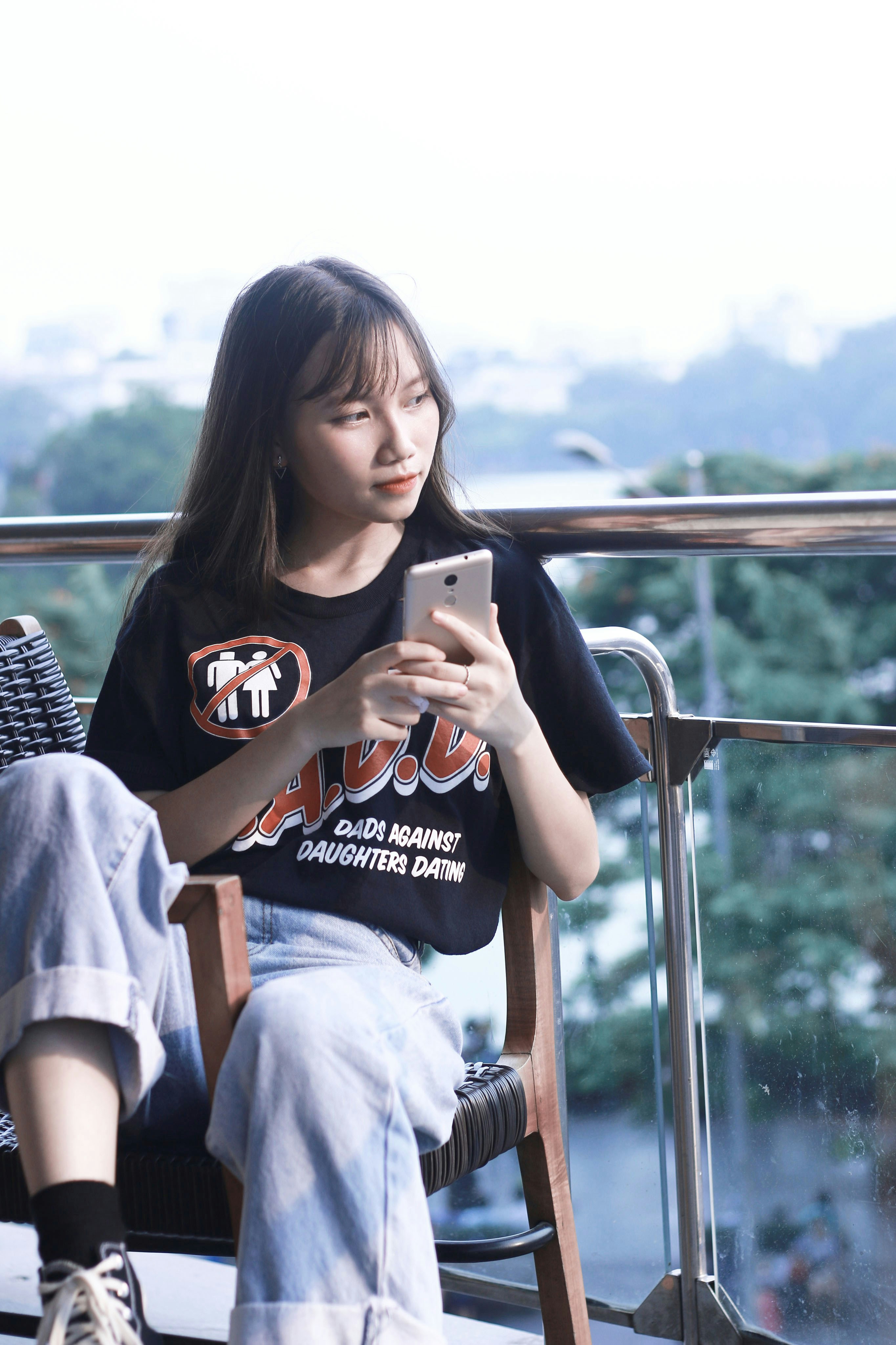 wanita duduk di kursi sambil memegang smartphone