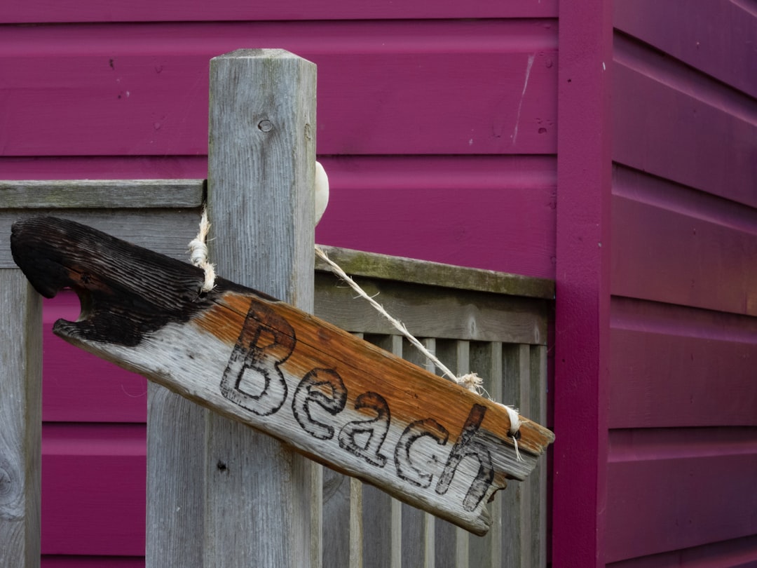 brown wooden signboard hanged in a fence near a purple wall