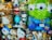 A display of various plush toys in a store window, including characters from popular animations. The toys are a mix of animals and cartoon figures, some of which are wrapped in plastic. Among them are a large green alien with big eyes, a brown bear, and several other colorful stuffed animals.