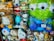 A display of various plush toys in a store window, including characters from popular animations. The toys are a mix of animals and cartoon figures, some of which are wrapped in plastic. Among them are a large green alien with big eyes, a brown bear, and several other colorful stuffed animals.