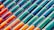 Rows of colorful ceramic tiles installed diagonally. The tiles display a gradient of colors ranging from vibrant orange to deep green. Each tile has a glossy finish, reflecting light in a playful manner.
