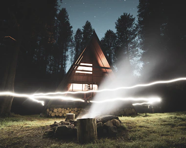 Warmly lit A-frame cabin nestled among tall pine trees at dusk.