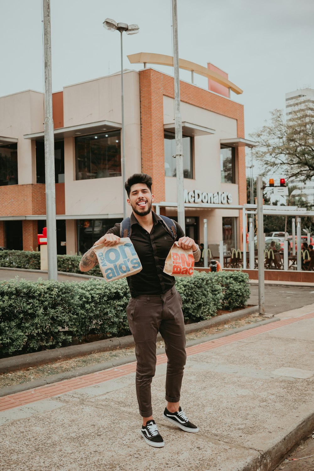 man wearing black dress shirt holding 2 MacDonalds paper bags