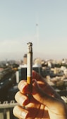 Close-up of a woman’s hand holding a lit cigarette against a foggy city night backdrop.