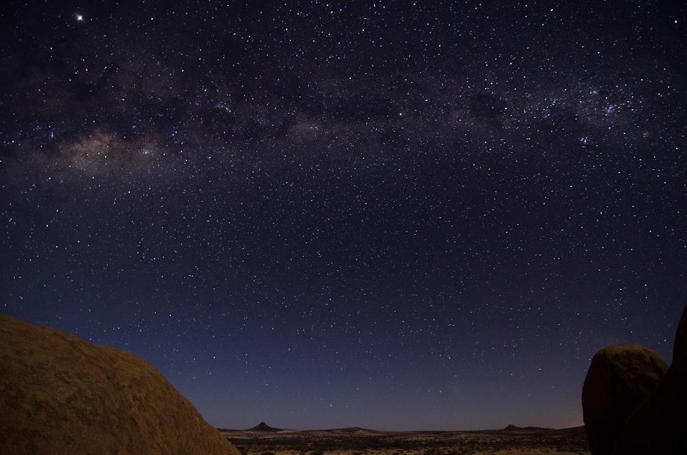 the night sky with stars above a rocky outcropping