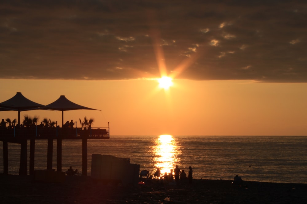 the sun is setting over the ocean with umbrellas