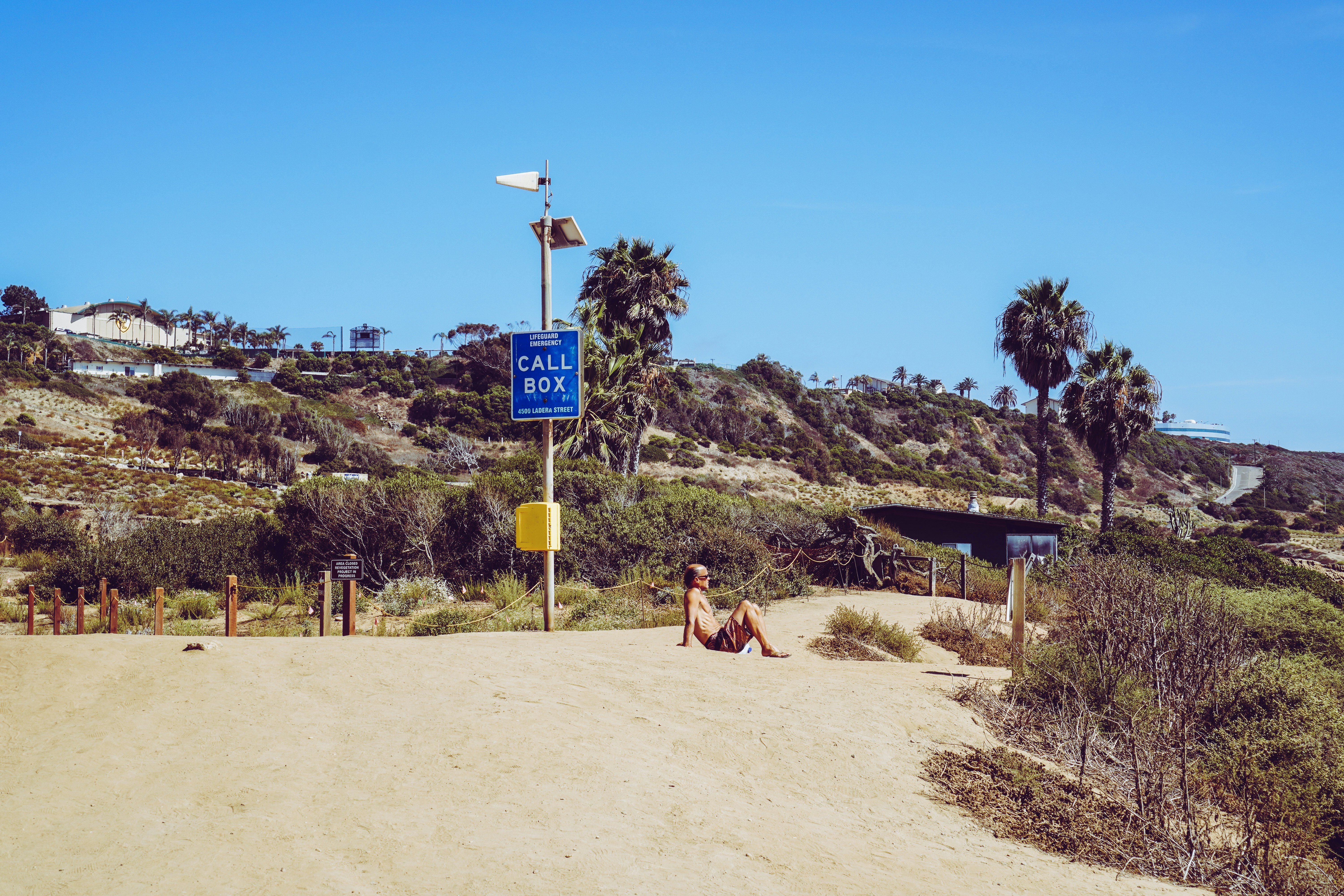 man sitting on sand beside signage