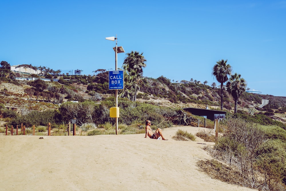 man sitting on sand beside signage