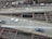 Aerial view of a multi-lane urban roadway with cars driving on two lanes. The infrastructure includes visible metal beams and supports underneath the road. Buildings and some greenery are seen in the background, indicating an urban setting.