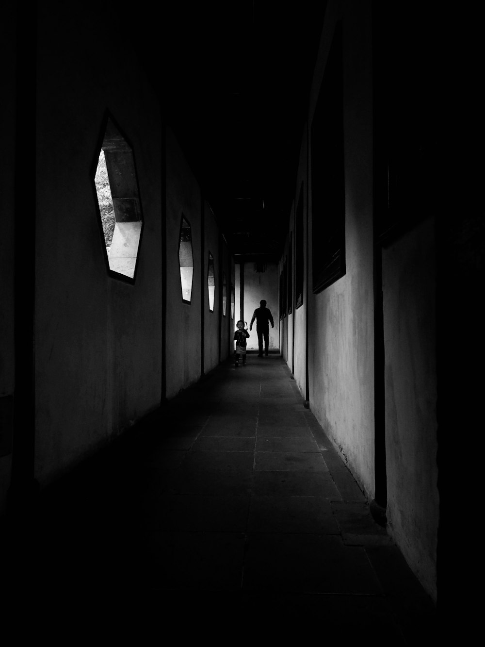 Photographie en niveaux de gris de deux personnes marchant dans le couloir