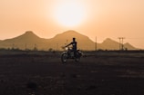 Sunset silhouette of a motorcyclist climbing a steep hill on the trail.