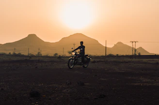 A rugged rider silhouetted against a fiery sunset over Mongolia’s vast steppe, with distant mountains framing the horizon.