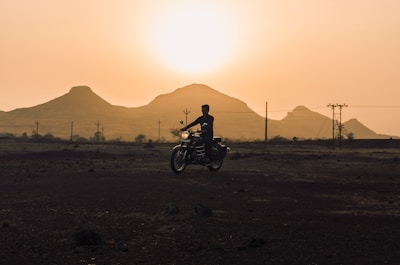 Sunset silhouette of a motorcyclist climbing a steep hill on the trail.