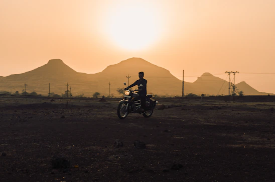 A rugged rider silhouetted against a fiery sunset over Mongolia’s vast steppe, with distant mountains framing the horizon.