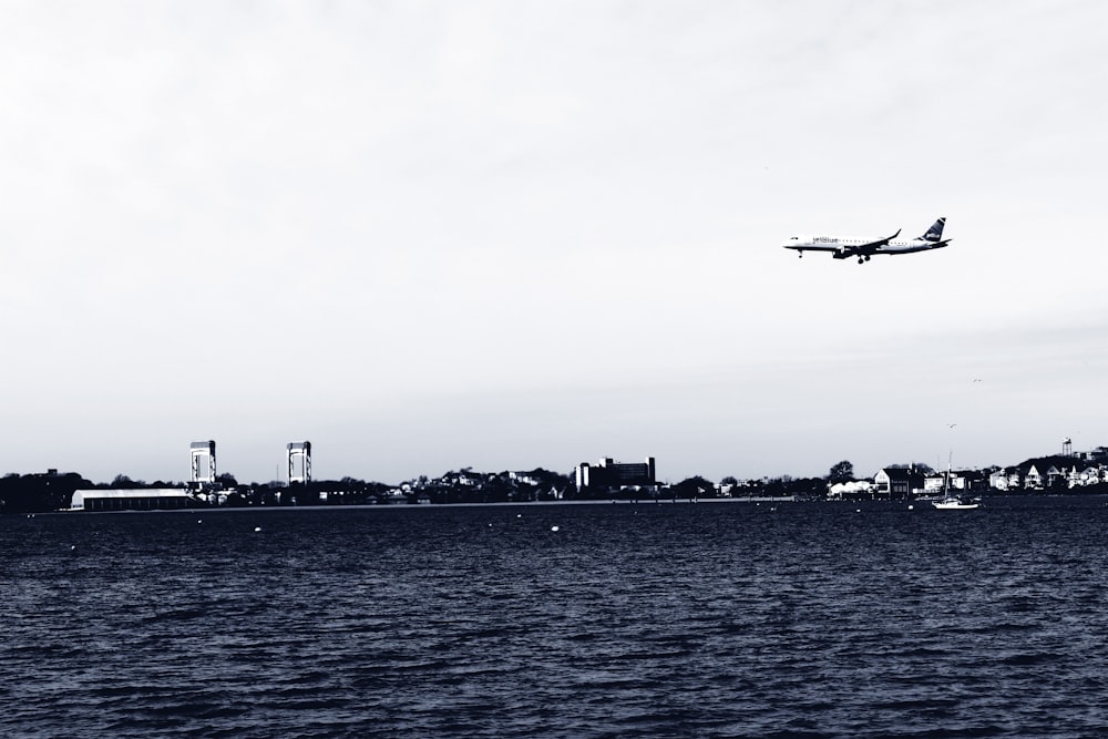 grayscale photography of airplane above sea viewing buildings