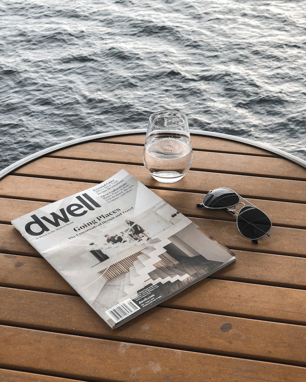 taza de agua junto a la revista y las gafas de sol